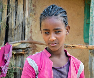 A girl in Ethiopia looks into the camera, wearing a pink jacket