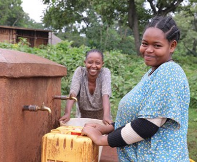 Two girls from Ethiopia filling up tubs of water.