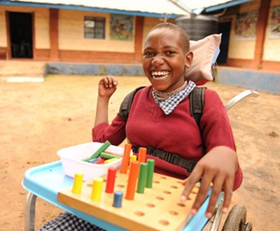 Girl from Kenya smiling while sitting in her wheelchair and playing with blocks