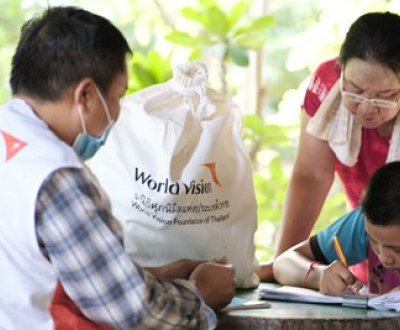 A boy writing something on his book in front of worldvision staff.