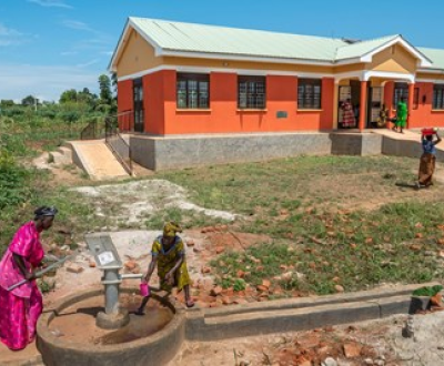 Woman getting water from a well with an orange building in the background