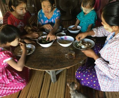 A woman from Myanmar and four children sitting in a circle on the floor around their dinner table and eating with their hands