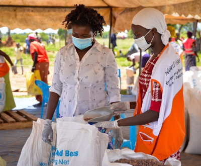 Female worker passes food over to another woman in an outdoor tent in Uganda