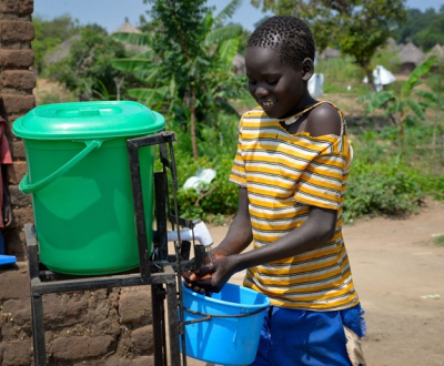 Ugandan boy holds hands underneath a hygiene station outdoors