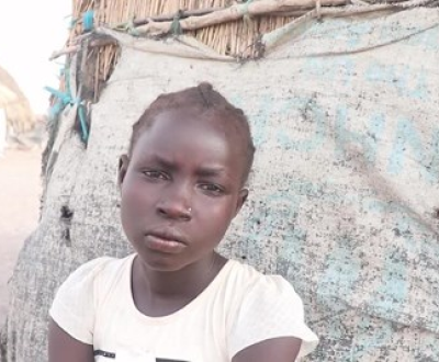 African girl sitting in front of a make-shift shelter.