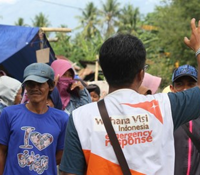 World Vision staff member waves with his back to camera in front of a crowd of people