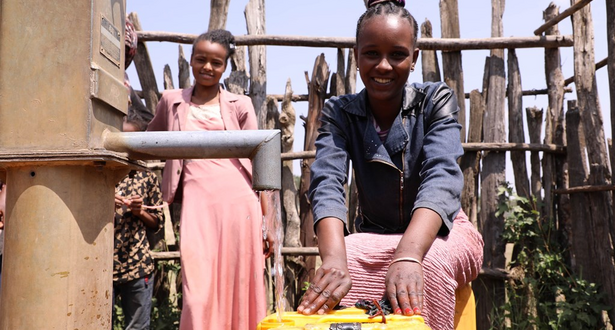 Girl from Ethiopia pours water from public tap into a yellow tub