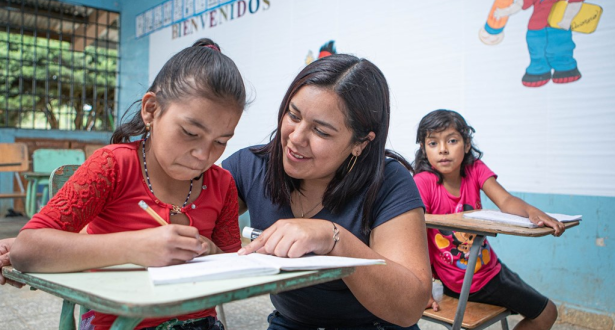 Teacher in Honduras helping a student with her work at her school desk