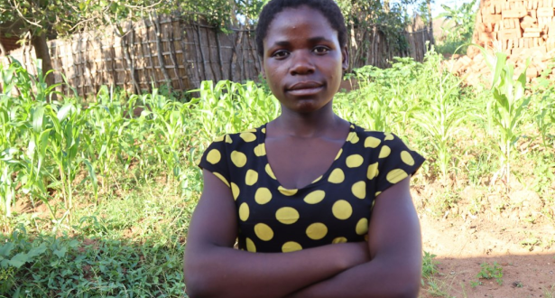 Girl from Malawi with her arms crossed looking at the camera while standing in a field