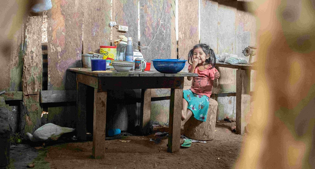 A girl child is siting inside a woode room on a wood stool near the table.