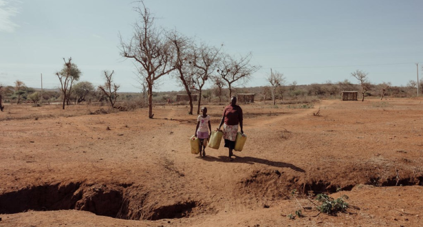 A mother and daughter walking through a dry land with cans in their hands