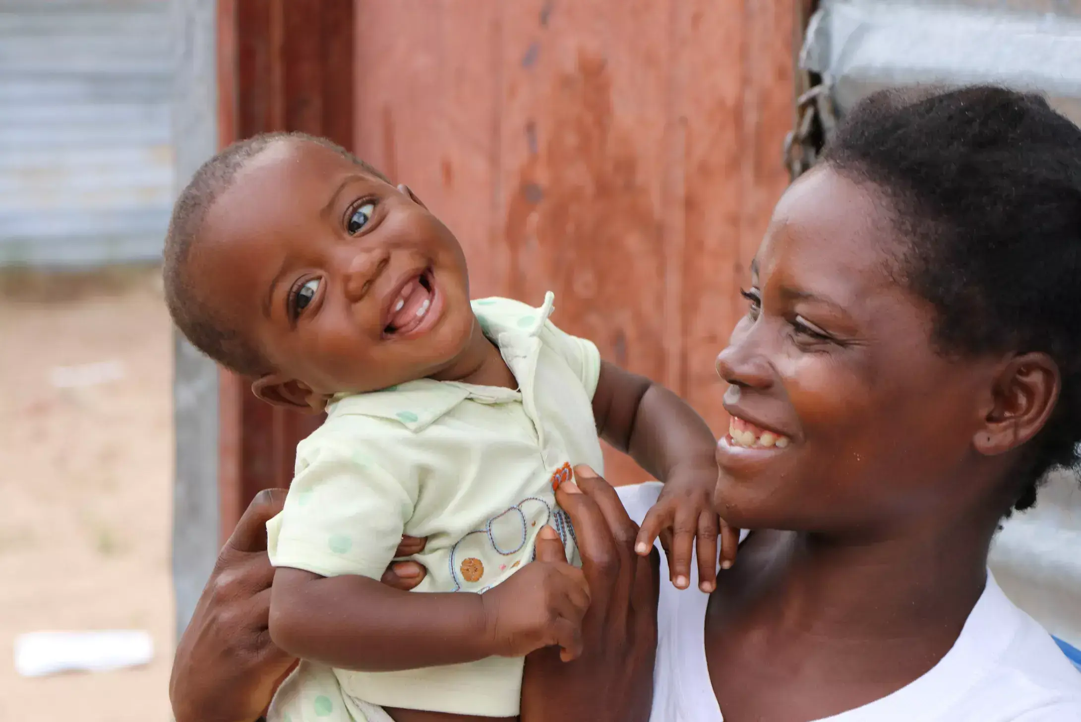 Boy from Angola smiles as he is held by his mother who is looking at him