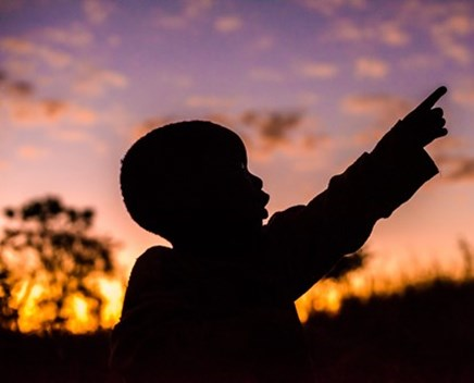 Child pointing up at sky, child in darkness, sunset behind