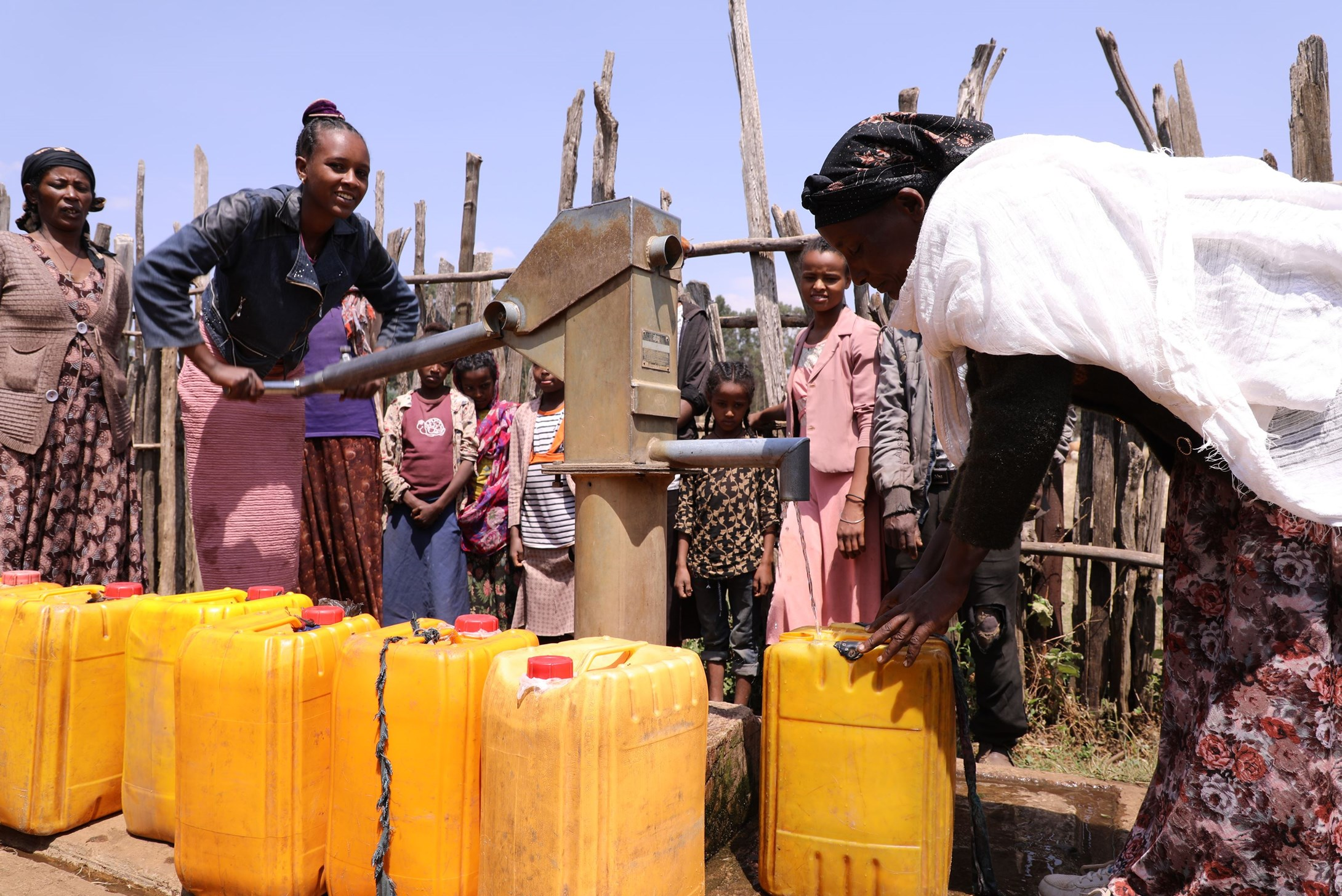 Girls and women from Ethiopia pictured filling up large yellow tubs with drinking water from their local public tap.