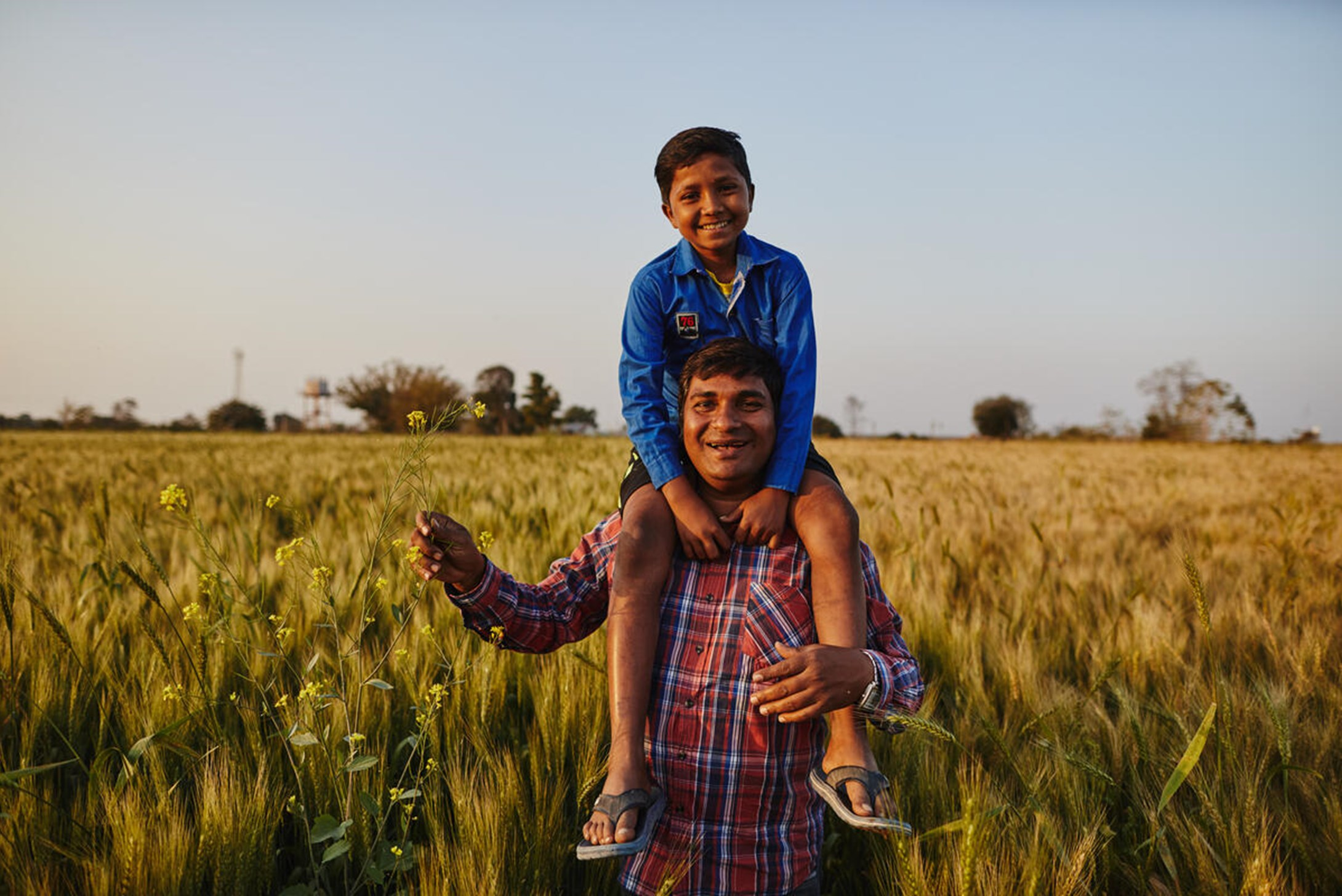 Father carrying his son over his shoulders in a field in India