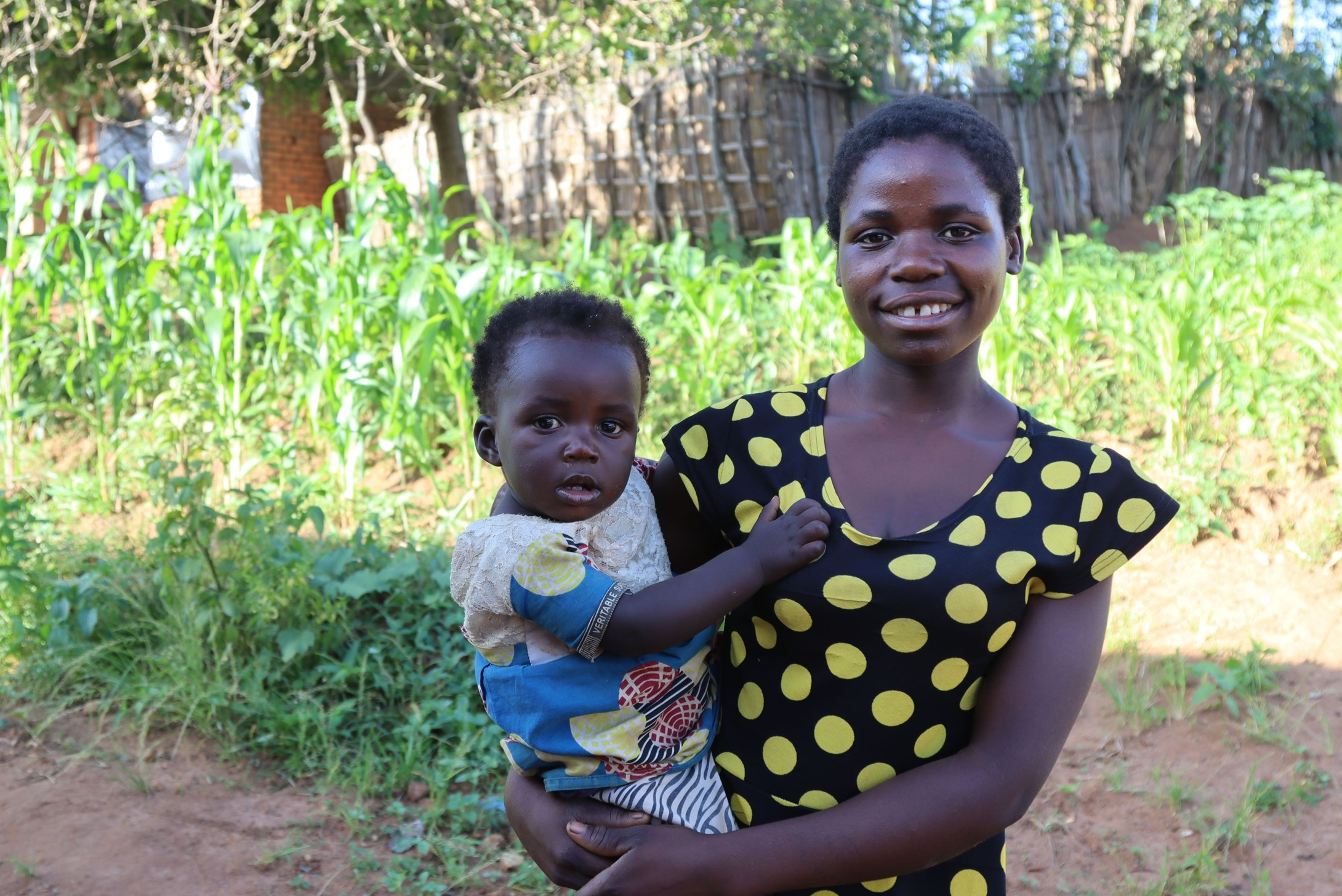 Girl from Malawi holding her 15-month toddler and smiling at the camera