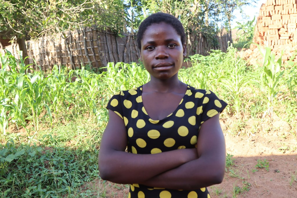 Girl from Malawi with her arms crossed looking at the camera while standing in a field