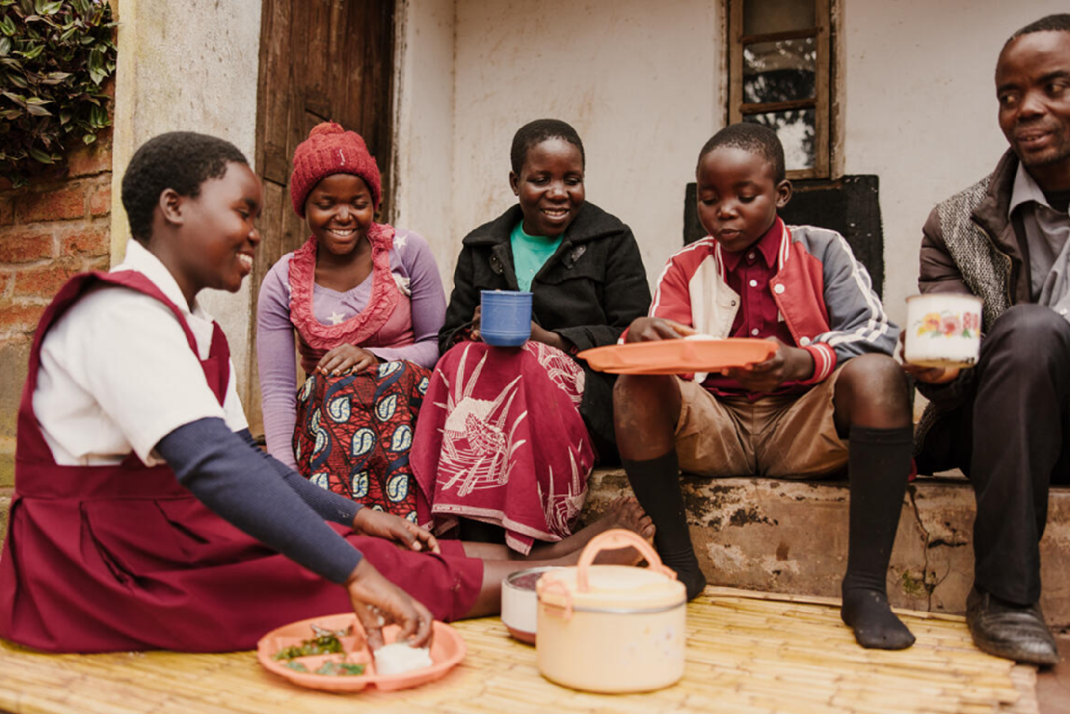 A family of five from Malawi sitting on the floor while eating and chatting.