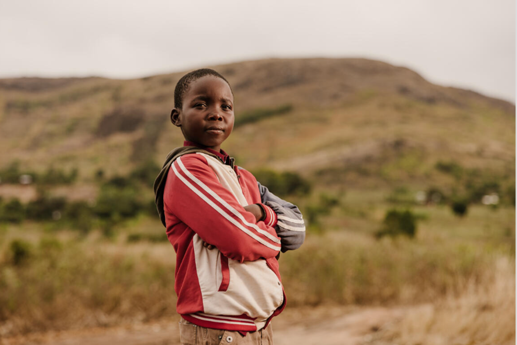 Boy from Malawi standing with his arms crossed in a field.