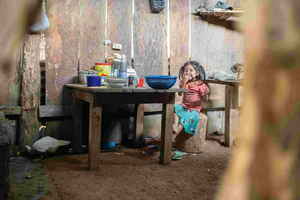 A girl child is siting inside a woode room on a wood stool near the table.