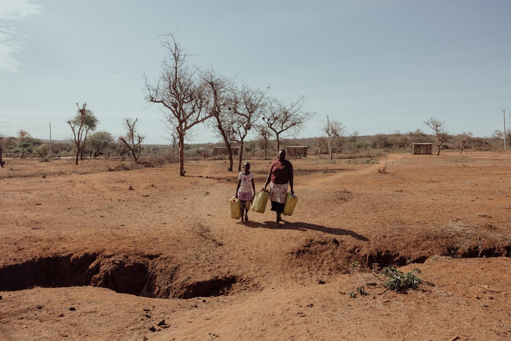 A mother and daughter walking through a dry land with cans in their hands