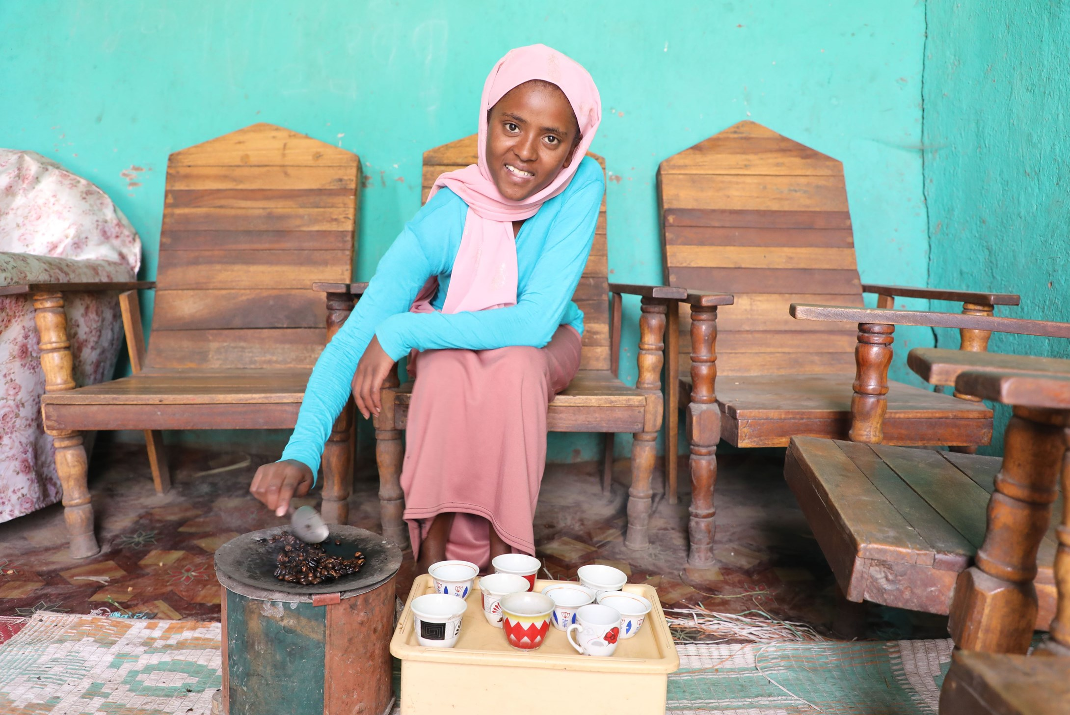 Girl from Ethiopia roasting coffee beans while smiling and looking at the camera 