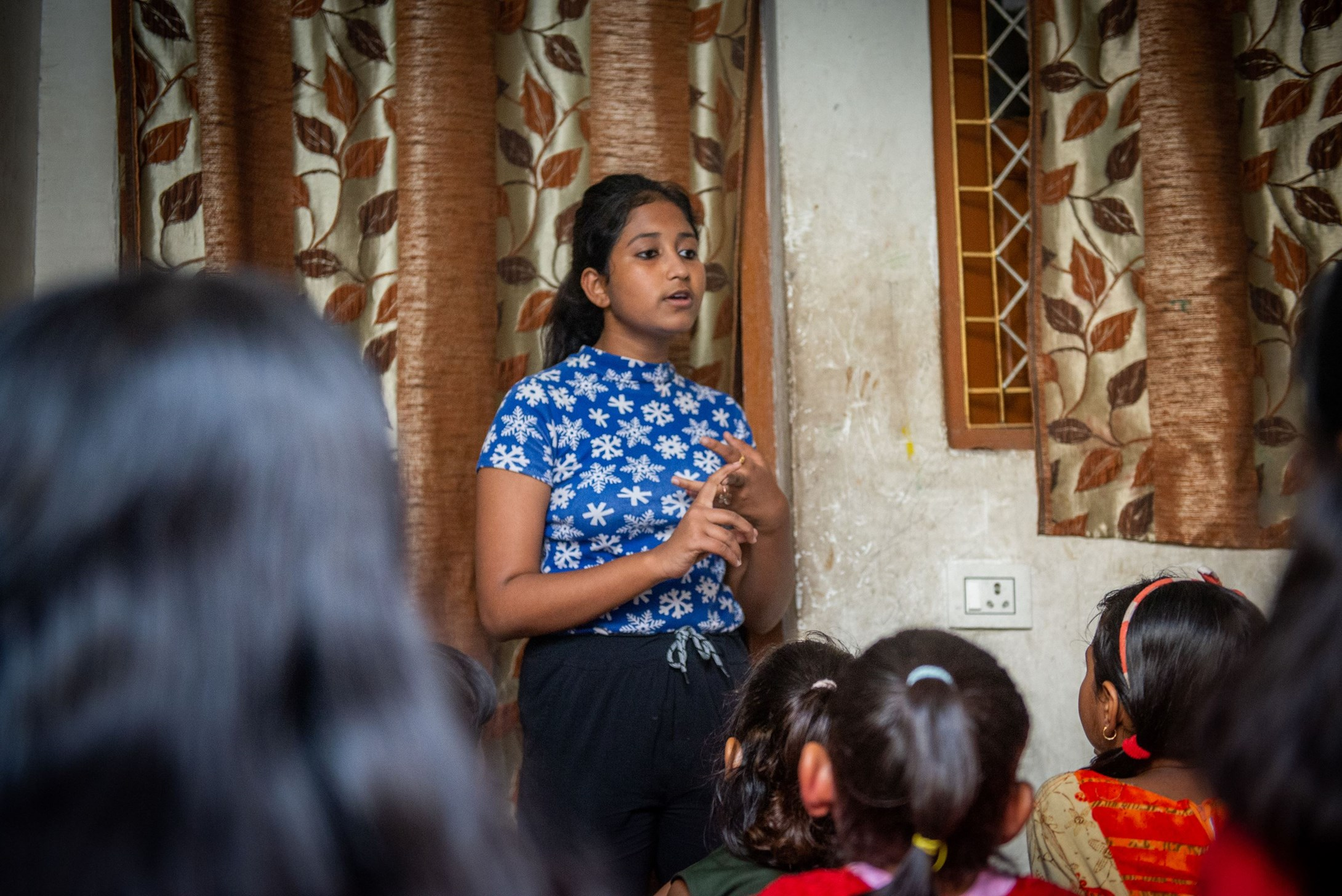 Girl from India educating a group of younger girls about gender violence sat on the floor in front of her.