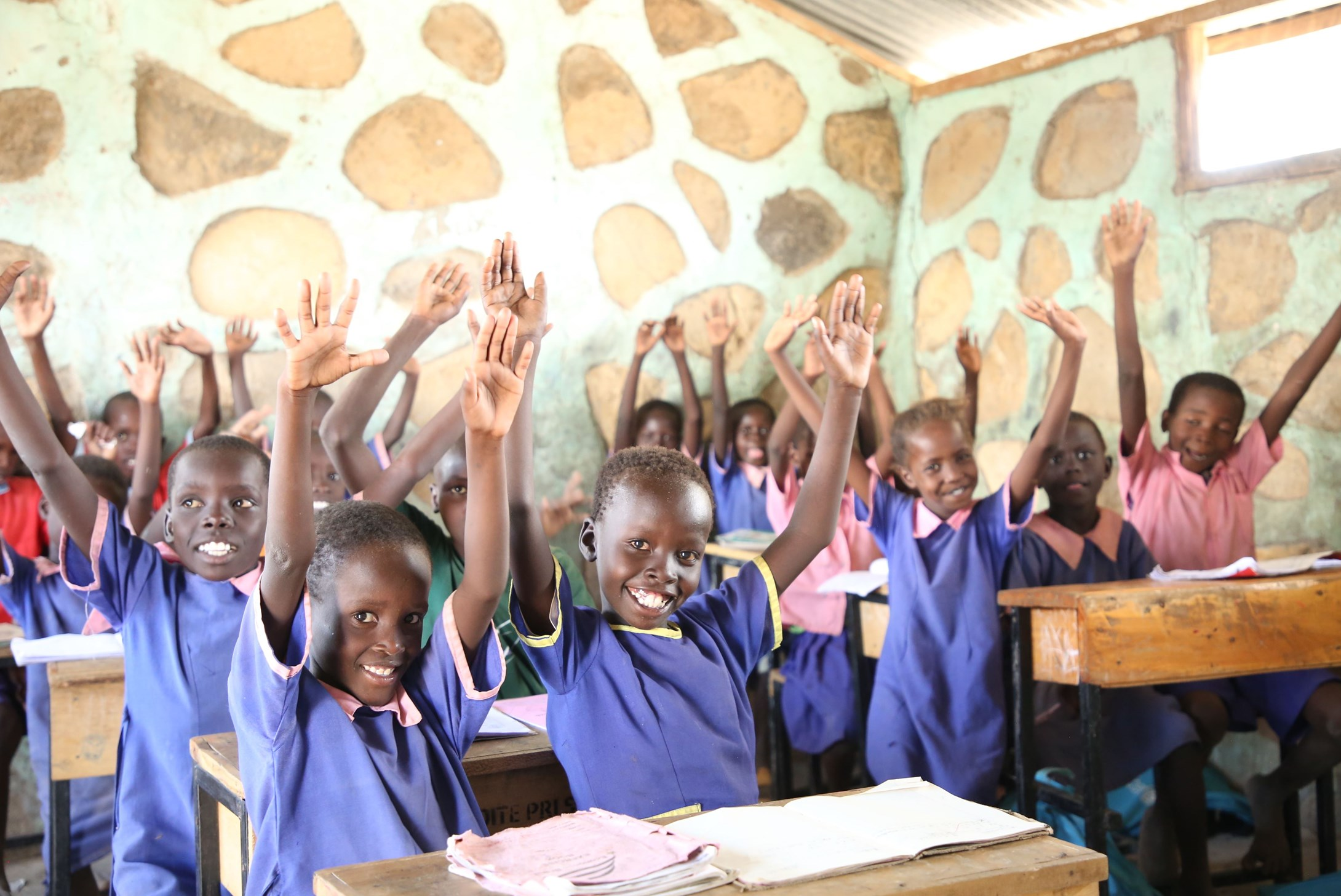 Classroom full of children raising their hands and smiling in Kenya