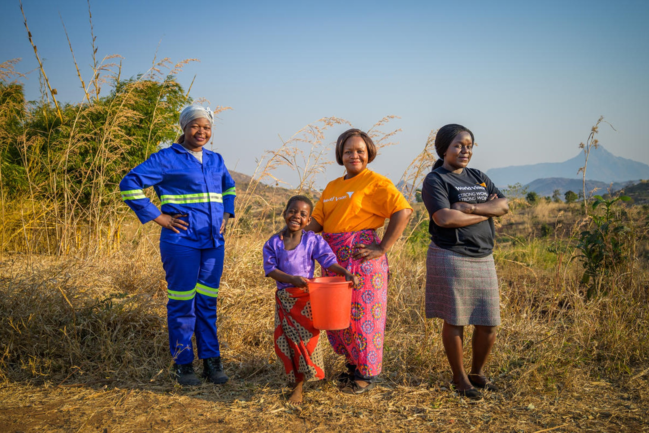 Women in Malawi with young girl and World Vision staff, standing proudly in field