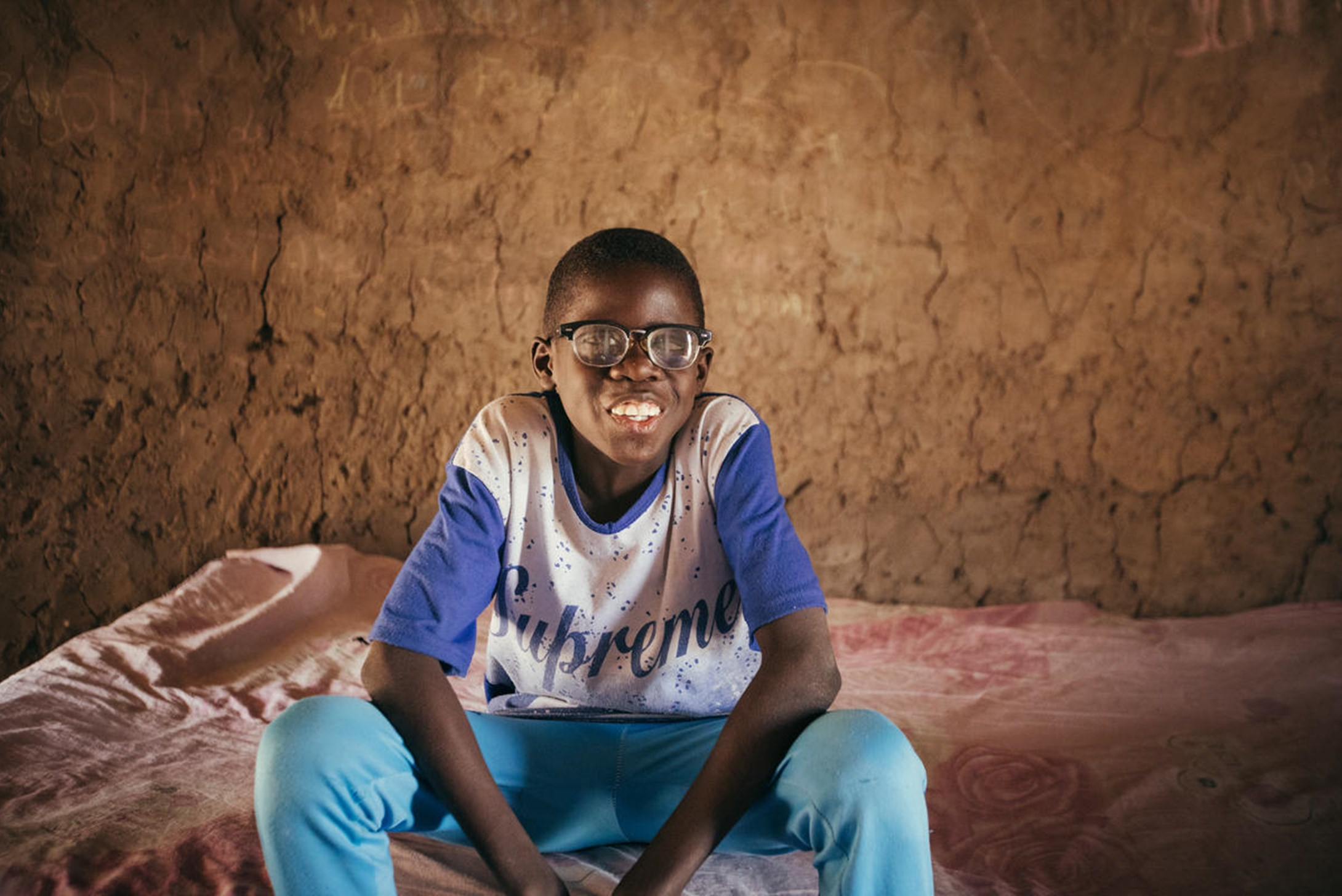 Boubacar, visually impaired boy sitting inside his house.